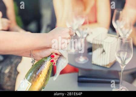 Une femme de gros plan ouvrant une bouteille de champagne blanc ou de prosecco à l'extérieur le jour d'été lumineux. Concept de fête des filles. Vie de luxe Banque D'Images