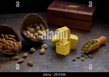 Pâtisserie indienne dessert, grains de cardamome dans une cuillère en bois, pistaches, amande et boîte en bois sur une surface de cuisine en béton. Banque D'Images