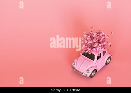 Changxing, Chine - 15 octobre 2019: Voiture rétro de jouet rose livrant bouquet de fleurs sur fond rose. Carte de Saint-Valentin 14 février Banque D'Images