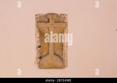 Ancienne croix de pierre avec des lettres INRI (Iesus Nazarenus Rex Iudaeorum - Jésus de Nazarath, roi des Juifs) dans le mur orange clair d'un bâtiment. Esso Banque D'Images