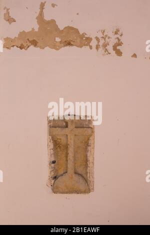 Ancienne croix de pierre avec des lettres INRI (Iesus Nazarenus Rex Iudaeorum - Jésus de Nazarath, roi des Juifs) dans le mur orange clair d'un bâtiment. Esso Banque D'Images