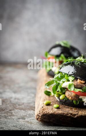 Champignons Veggie, salade verte et hamburgers noirs de légumes. Sur fond de pierre grise Copyspace. Banque D'Images