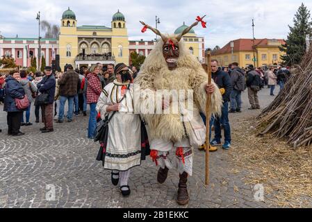 Un buso masqué et une femme traditionnelle vêtue marchant dans la procession lors de la célébration du carnaval Busojaras de 2020 à Mohacs, en Hongrie Banque D'Images