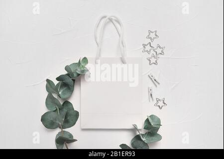 Cadre en feuilles d'eucalyptus et paquet blanc sur fond blanc. Couronne faite de branches de feuilles. Maquette d'une pose plate, vue de dessus avec place pour votre texte Banque D'Images