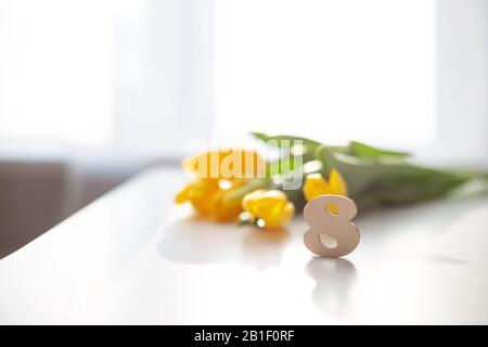 Le nombre de bois huit est sur une table blanche. Derrière dans la mise au point douce se trouve un bouquet de tulipes jaunes. Journée Internationale De La Femme . Espace de copie Banque D'Images