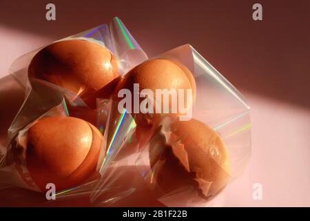 Œufs bruns de poulet en feuille transparente aux reflets colorés. Concept futuriste de vacances de Pâques minimales à la mode. Banque D'Images