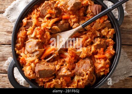 Le chou savoureux est cuit avec de la viande, des tomates, des carottes et des oignons dans une poêle sur la table. Vue de dessus horizontale Banque D'Images