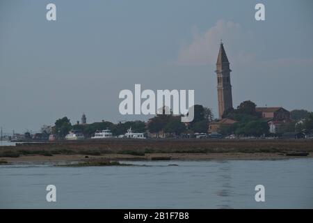 Les bateaux amarrés de l'île Burano et Chiesa di San Martino penché sur le clocher de l'église du XVIIe siècle vu de la lagune à travers les marais salants, Venise, Italie Banque D'Images