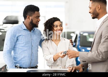 Le Concessionnaire De Voiture Donne La Clé Au Couple En Position Debout Dans Le Centre De La Concession Banque D'Images
