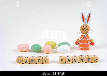 Blocs en bois avec des lettres disant "Joyeuses Pâques" devant des oeufs de pâques colorés et un lapin de pâques sur fond blanc avec espace de copie Banque D'Images