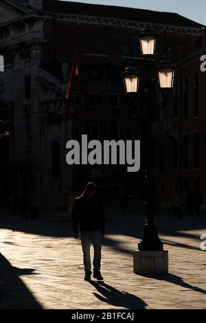 Silhouette d'un homme marchant dans une rue de Venise (Italie), lampadaire illuminé par le soleil Banque D'Images