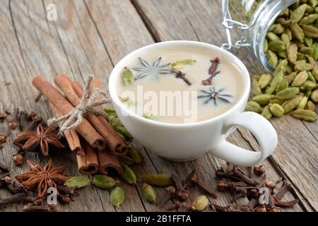 Tasse de thé ou de café ayurvédique sain avec du lait et des épices aromatiques. Bâtons de cannelle, cardamome, clous de girofle et étoiles anis sur table. Banque D'Images