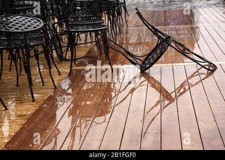 Meubles de restaurant sous la pluie. Chaises sur sol en bois humide. Scène urbaine sur fond humide. Banque D'Images