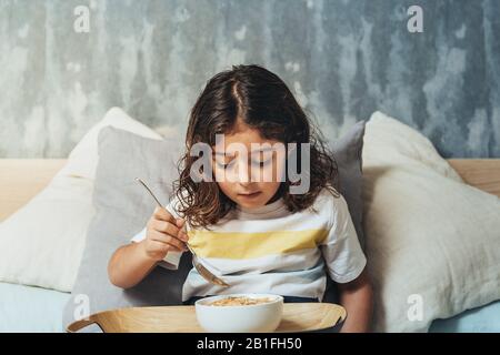 petite fille avec petit déjeuner le dimanche dans le lit de ses parents. Enfant profitant d'un bol de céréales à la maison le matin, concept de mode de vie sain et foo Banque D'Images