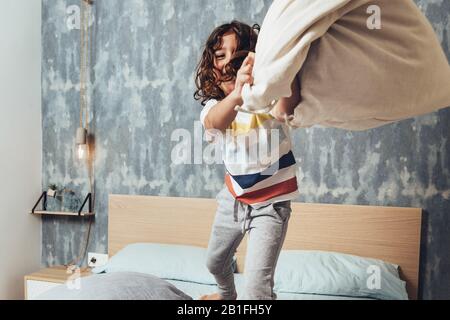 drôle petite fille jeter un coussin debout sur son lit de parents, concept de style de vie à la maison et une enfance heureuse Banque D'Images