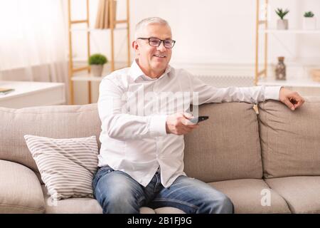 Homme âgé regardant la télévision assis sur un canapé Banque D'Images