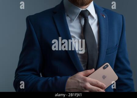 Zaporozhye. Ukraine. Février 2020. Gros plan portrait d'un jeune homme barbu dans un costume d'affaires tenant un iPhone XS dans sa main. Nouveau smartphone de Banque D'Images