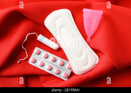 Tampon sanitaire, tampon, pilules et coupe menstruelle sur fond rouge, vue de dessus Banque D'Images