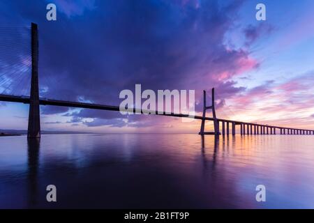 Un lever de soleil coloré derrière le pont Vasco da Gama, reflété sur le Tage. Lisbonne, Portugal, Europe. Banque D'Images