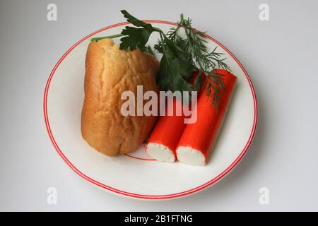Toujours la vie d'un morceau de pain blanc, de bâtonnets de crabe et de persil sur une plaque blanche avec une bordure rouge. Stock photo pour le web et l'impression, le papier doré et l'arrière-plan. Banque D'Images