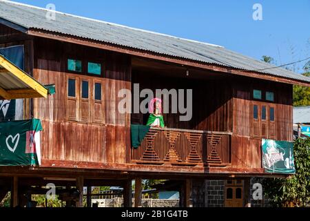 Une Femme Du Groupe Minoritaire De Kayan (Longneck), Debout Sur Un Balcon D'Une Maison Traditionnelle En Bois, Loikaw, État De Kayah, Myanmar. Banque D'Images