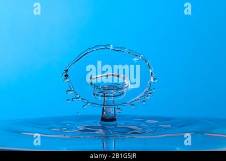 Photo abstraite d'une collision avec une goutte d'eau créée avec deux gouttes d'eau qui éclaboussent ensemble isolée sur un fond bleu. Banque D'Images