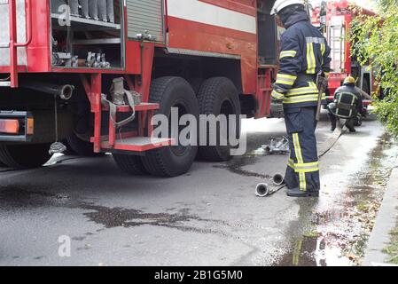 Les pompiers travaillent dans une source d'inflammation dans un immeuble résidentiel. Les gens en uniforme va décompresser la lance à incendie, le préparant pour éteindre le sapin Banque D'Images