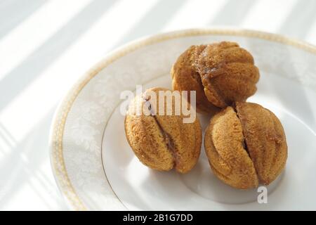 Trois petits cookies sous forme de noix sur une soucoupe blanche et une table ensoleillée. Banque D'Images