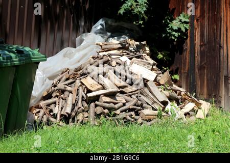 Pile de bois de chauffage fraîchement coupé empilée sur le nylon transparent et l'herbe non coupée dans le coin de la maison familiale de banlieue arrière-cour entourée de grand bois Banque D'Images