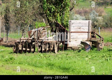 Divers équipements agricoles anciens et rustiques rétro, anciens et abandonnés, délabrés, avec remorque de tracteur en bois cassée laissée dans le dos de la maison familiale de banlieue Banque D'Images