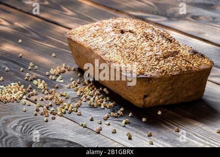 Le pain de sarrasin sans gluten avec croûte brune dorée, saupoudrée de graines de sésame, se trouve sur une table en bois. Recette maison saine. Grains de vert Banque D'Images