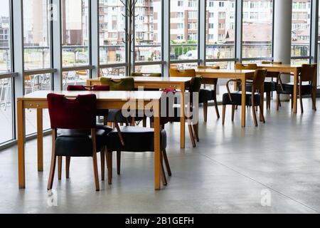 Des tables en bois vides et des chaises en cuir se trouvent près des fenêtres panoramiques. Aire de restauration. Banque D'Images