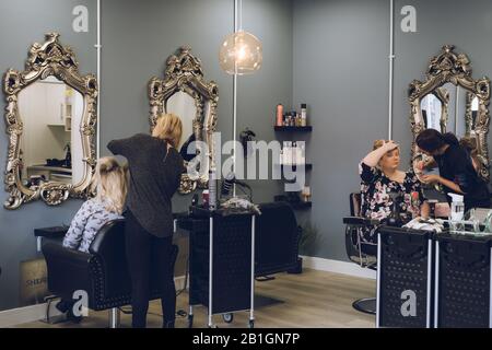 L'intérieur d'un salon de coiffure avec un coiffeur coiffant les cheveux et un artiste de maquillage appliquant le maquillage Banque D'Images