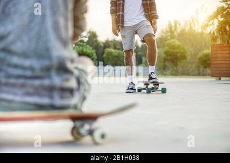 Deux skate-boarders s'entrainent dans le skate Park au coucher du soleil - gros plan de l'entraînement des jeunes tatoueurs avec planche à roulettes dans le concours urbain de la ville - Extreme sport concepp Banque D'Images