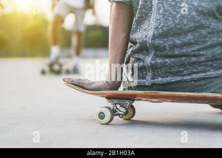 Gros plan de jeune homme assis sur le skateboard à la recherche de son ami entraînement extérieur - Skateboarder se préparant à sauter dans le concours urbain - la conce de sport extrême Banque D'Images