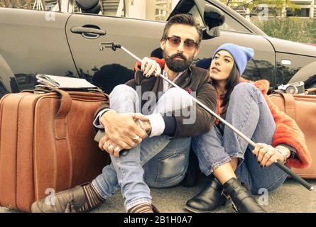 Hipster couple assis sur la rue à côté de leur cabrio - Femme embrassant son homme avec bâton dans les mains - Voyage et mode de vie concept - désaturer Banque D'Images