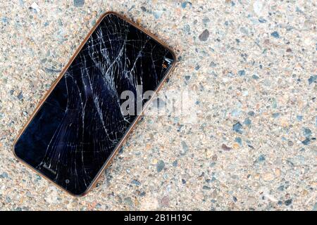Un téléphone portable cassé et cassé posé sur un trottoir en béton. L'écran du téléphone portable est cassé et brisé. Le téléphone n'est pas identifiable. Banque D'Images