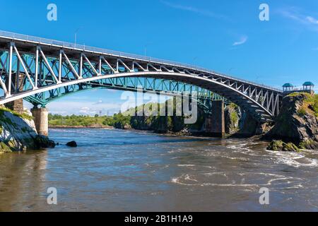 Le pont Reversing Falls à Saint John, au Nouveau-Brunswick, au Canada, au-dessus de la rivière Saint John. Rivière qui coule lentement. Pont de train derrière, ciel bleu au-dessus. Banque D'Images