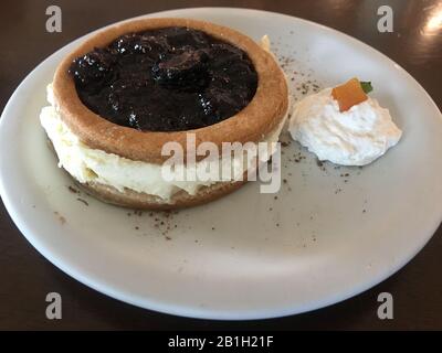 Gros plan sur un délicieux cheesecake blackberry avec crème fouettée et abricot dans le coin de la plaque de céramique blanche sur une table en bois. Banque D'Images
