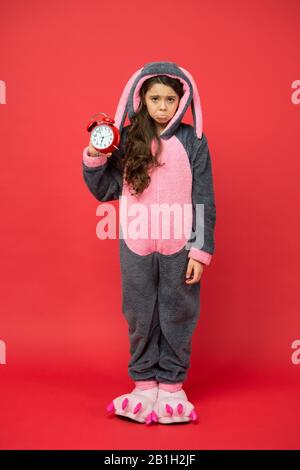 Jour normal de début. Adorable réveil à motif lapin. Petite fille en costume de lapin. Enfant lapin kigurumi. Pyjama fille à motif lapin. Bunny rouge enfant fond. Bébé animal. Temps de comptage. Alarme du matin. Banque D'Images