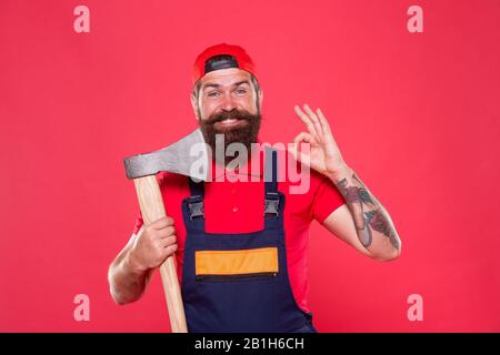 forester tenir la hache. l'homme en uniforme couper les cheveux de barbe avec la hache. l'homme barbu brutal utiliser la hache. Randonnée vacances. Assez courageux. Mieux utiliser la lame dans le barbershop. Brutal et barbu. L'homme montre un geste ok. Banque D'Images