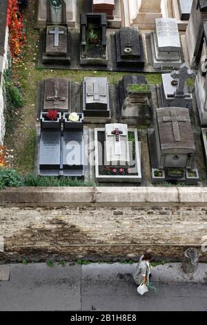 Vue imprenable sur une femme marchant au mur du cimetière de Montmartre avec le cimetière de Montmartre en arrière-plan.Paris.France Banque D'Images