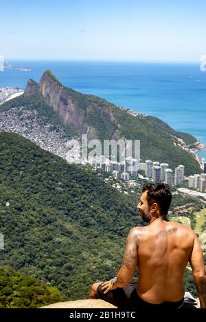 Homme vu de derrière profitant de la vue du point de vue de Pedra Bonita regardant sur le quartier de São Conrado avec les Deux frères montagne Banque D'Images
