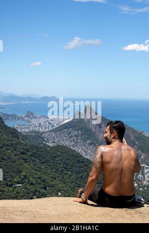 Homme vu de derrière profitant de la vue du populaire point de vue de randonnée Pedra Bonita regardant sur le quartier de São Conrado avec les Deux frères Banque D'Images