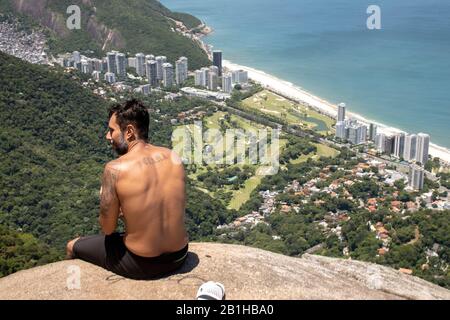 Homme vu de l'arrière profitant de la vue du populaire point de vue de randonnée Pedra Bonita regardant sur le quartier de São Conrado avec un terrain de golf Banque D'Images