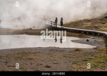Touristes sur un chemin en bois regardant la vapeur de source chaude dans le brouillard. Banque D'Images