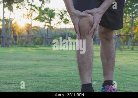 Les blessures au genou. Sport Jeune homme tenant le genou avec ses mains dans la douleur après avoir subi une lésion musculaire au cours d'une exécution de l'exercice dans parc. Les soins de santé et spor Banque D'Images