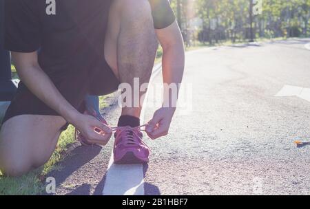 L'athlète masculin noue des lacets de chaussures de course dans le parc à la lumière du soleil se prépare à faire du jogging dans le jardin. Concept de sport et d'exercice. Banque D'Images