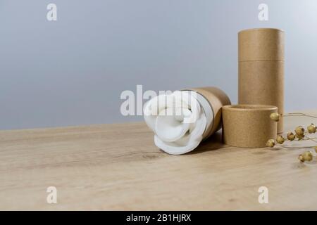 Tube en papier ou en carton avec disques en coton blanc à l'intérieur sur fond en bois. Recyclage concept de réutilisation de tubes d'emballage en carton pour cosmétiques naturels Banque D'Images