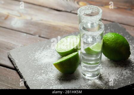 Tequila argent projectiles avec des tranches de citron vert et sel sur planche en bois Banque D'Images